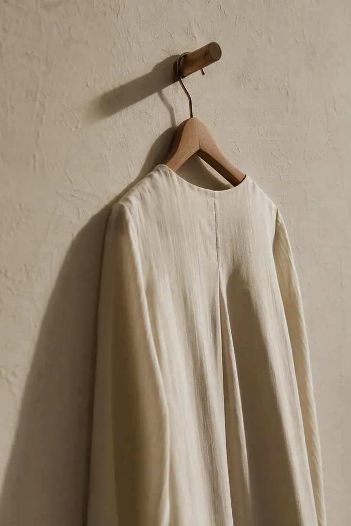 The signature blouse on a wooden hanger against plaster